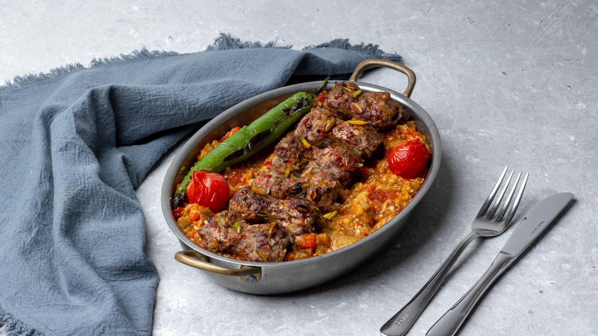 Köfte baked in a copper pan with tomato, green chilli and pistachio