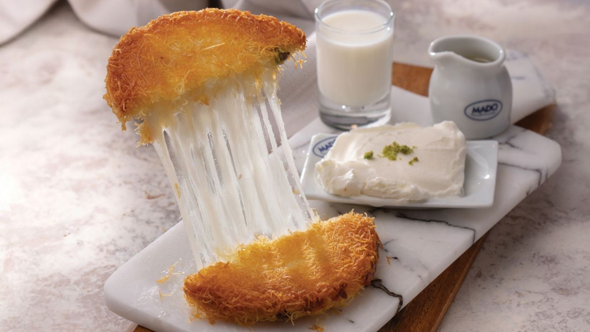 Künefe pulled apart showing stretchy cheese, served with kaymak and milk